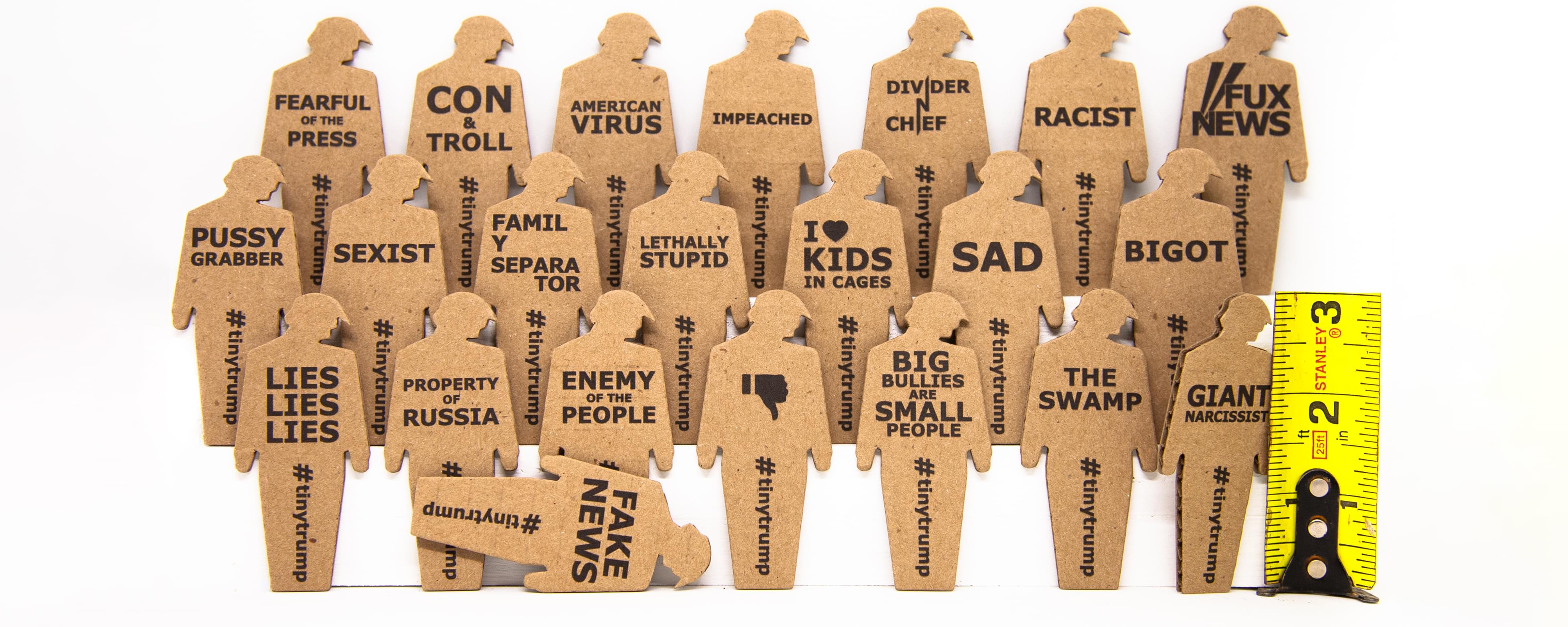 tiny trumps are three inch tall cardboard cutouts of President trump with protest slogans stamped on the chest and '#tinytrump' running down the middle of the figure's legs. Shown on the right is a yellow ruler with a tiny trump leaning against it, indicating the tiny trump is three inches tall.