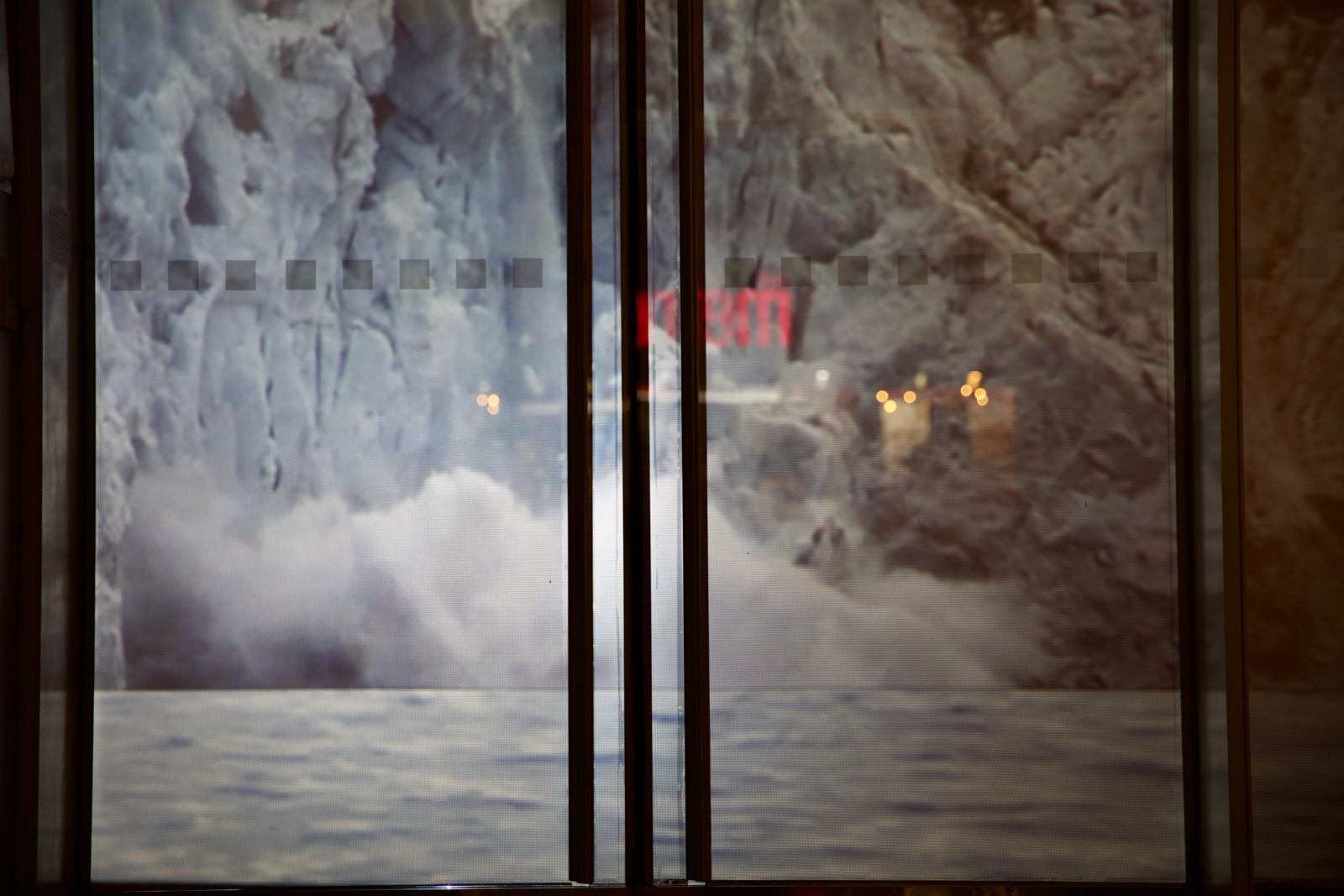 Closeup of the buiding's storefront windows showing a projected image of a large glacier collapsing into a body of water. The image is pixellated since it is so close-up.