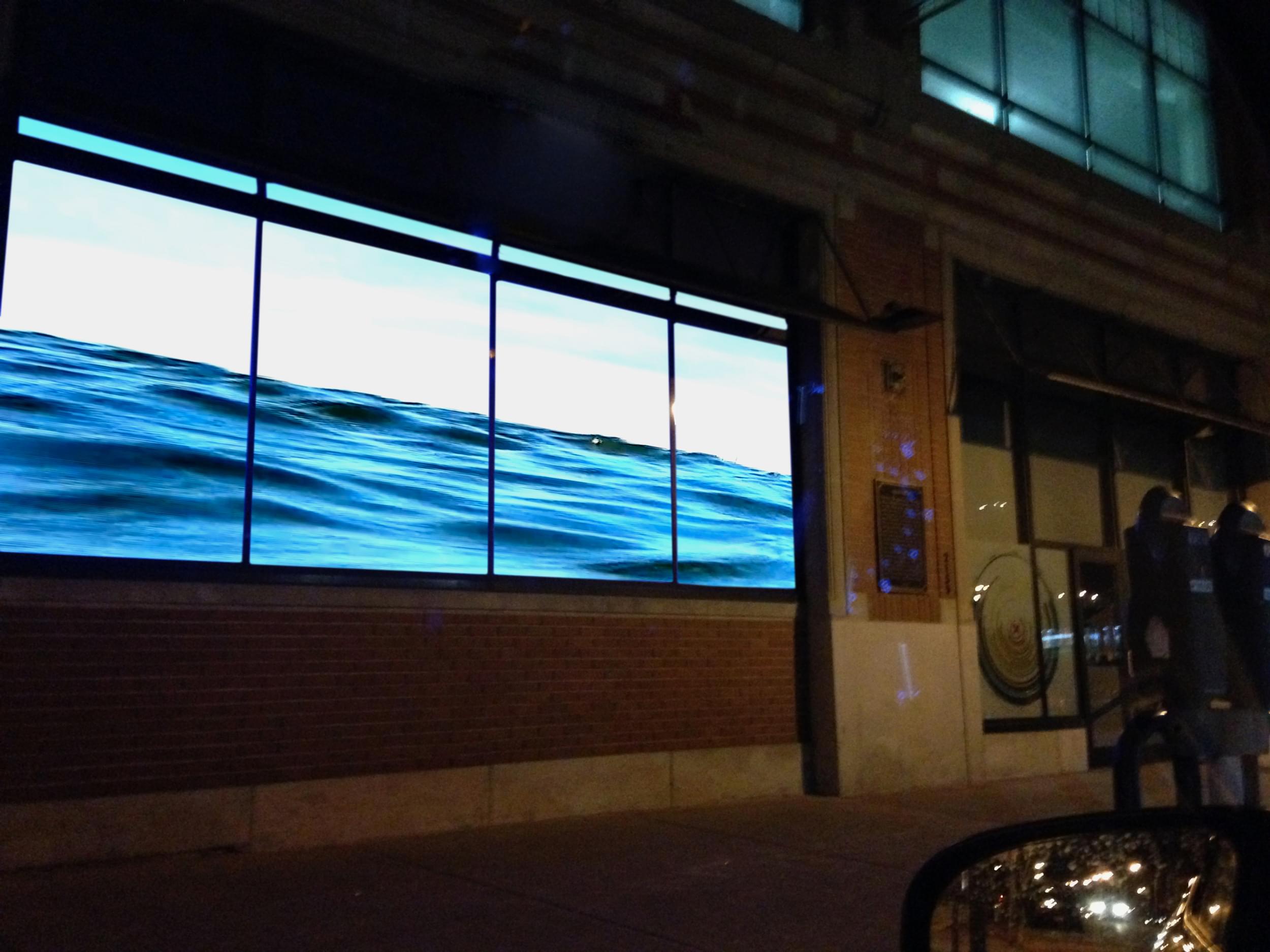 Nighttime photograph of a body of water projected into the storefront windows of a gallery