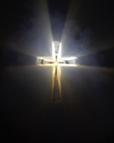 Photograph of a crucifix, hovering in mid-air and being formed solely by light. It is cloudy around the edges, and there is a sharp circular focus of light in the middle from whence the light is shone.
