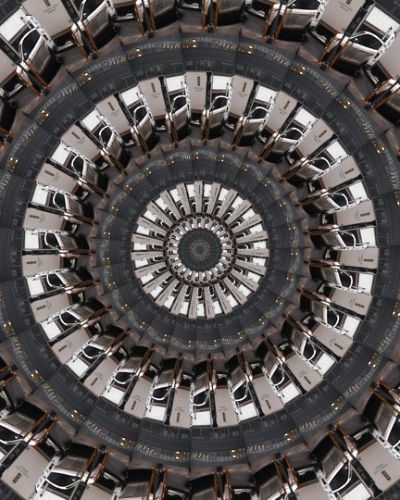Algorithmically generated kaleidoscopic image consisting of a series of infinite-mirror-esque concentric discs, each one subdivided into multiple tranches that show the same image, albeit rotated by a consistent amount across the disc. In this case, the image that gets repeated across all discs at different angles is a photograph of a white SUV in front of a white delivery truck.
