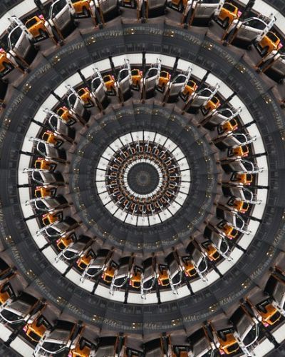 Algorithmically generated kaleidoscopic image consisting of a series of infinite-mirror-esque concentric discs, each one subdivided into multiple tranches that show the same image, albeit rotated by a consistent amount across the disc. In this case, the image that gets repeated across all discs at different angles is a photograph of two parked cars abutting each other, one NYC yellow cab and the other a white van.