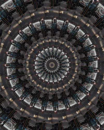 Algorithmically generated kaleidoscopic image consisting of a series of infinite-mirror-esque concentric discs, each one subdivided into multiple tranches that show the same image, albeit rotated by a consistent amount across the disc. In this case, the image that gets repeated across all discs at different angles is a photograph of the blue cab of an 18-wheeler in front of a white delivery van.