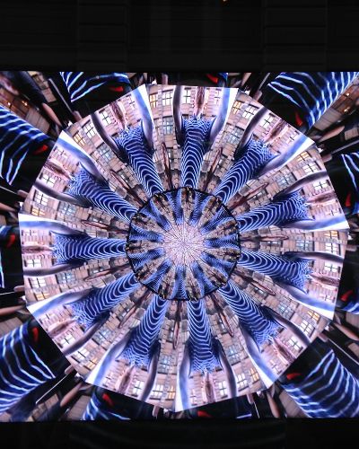 Photograph of a screen showing a kaleidoscope of infinite-mirror-esque concentric discs, each one subdivided into multiple tranches that show the same image, albeit rotated by a consistent amount across the disc. In this case, the image that gets repeated across all discs is a person&rsquo;s black and white striped t-shirt, lending the overall image a very zebra-stripe-like quality.