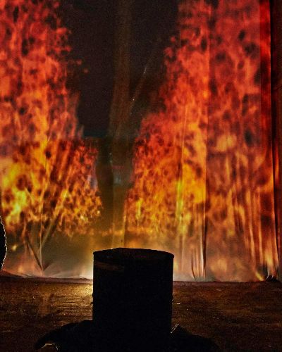 Night time photograph; tunnel; medium shot of the silhouetted backs of two men; approximately 15 feet in front of them (a projection of) a raging fire, approximately 20 feet tall, presented in sharp 1 point perspective so as to appear to be going on forever into infinity