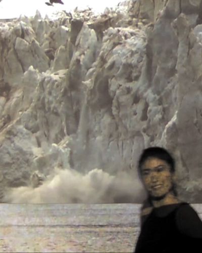 A viewer smiles at the camera as she walks in front of a video projection of a collapsing glacier