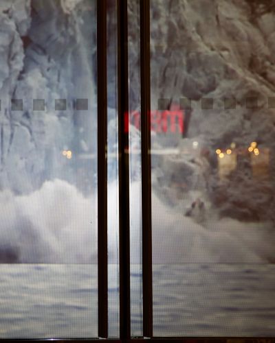 Closeup of the buiding's storefront windows showing a projected image of a large glacier collapsing into a body of water. The image is pixellated since it is so close-up.