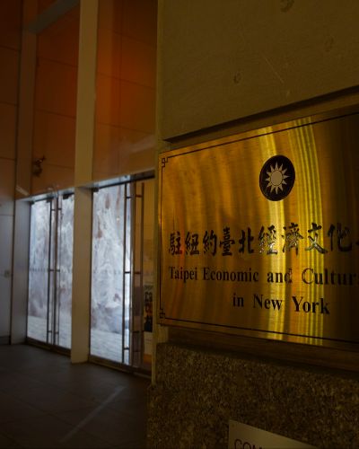 Close up nighttime photograph of the signage of the building in the previous photograph. The signage (a medium-sized gold plate) reads 'Taipei Economic and Cultural Office in New York.'  Blurred in the background is a projection of glaciers in the building's storefront windows.