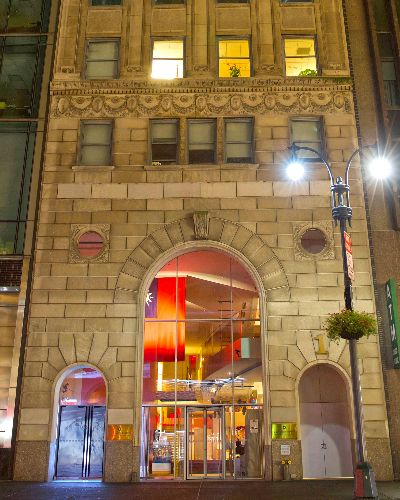 Extremely tall vertical photograph that encompasses approximately 15 stories of the facade of a beige apartment building. On street level, projected into the windows of the building's entrance, is an Arctic landscape with a large glacier in the middle of the frame.