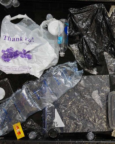 Close-up, top-down photograph of about three dozen single-use plastic items floating on a black body of water. Most prominently featured is a white plastic 'Thank You' shopping bag.