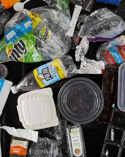 Top-down close-up photo of about 50 pieces of trash floating in a black pool. Most prominently featured is a yellow Polar Seltzer bottle, Bounty plastic wrapping, and an Amazon Prime shipping package.