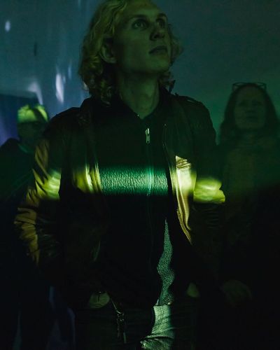 Photograph of a viewer, coated in yellow light with a particularly bright band of yellow light flowing horizontally across his chest, looking upward, with curiosity
