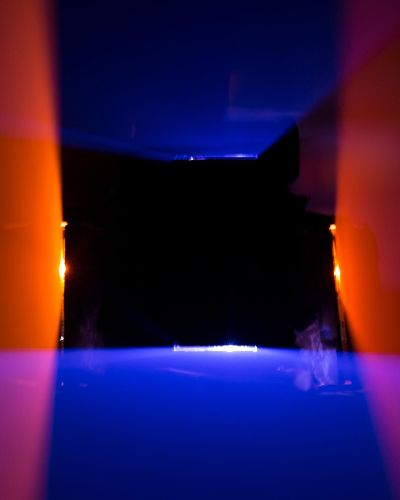 Very strange photograph of a rectangular black hole in the middle, about the size of a cafeteria lunch tray. Emanating from the top and bottom of the rectangular black hole are blue rhomboid planes of light that get wider as they approach the viewer. Emanating from the left and right sides of the rectangular black hold are red-orange rhomboid planes of light that also get wider as they approach the viewer.