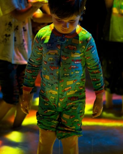 Nighttime photograph of a small child in pajamas looking down is illuminated by an orange light emanating from the colorful surface of the pool he is standing in