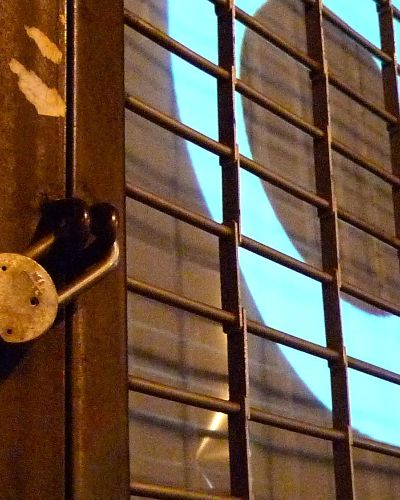 Nighttime, close-up photograph of two large, cartoonish eyes projected into a storefront window behind a metal security gate