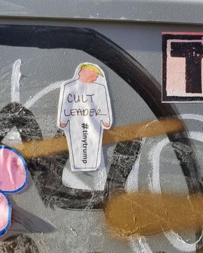 Photograph of a white 'DIY' tiny trump printed on label paper with the words Cult Leader handwritten in pen