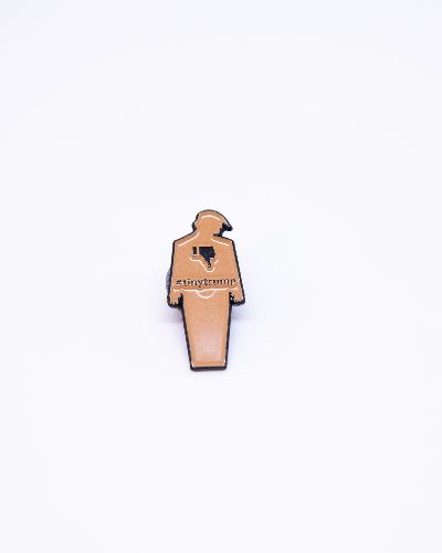 Photograph of a brown tiny trump enamel pin with a thumbs down sign on the left lapel of a man's suit blazer