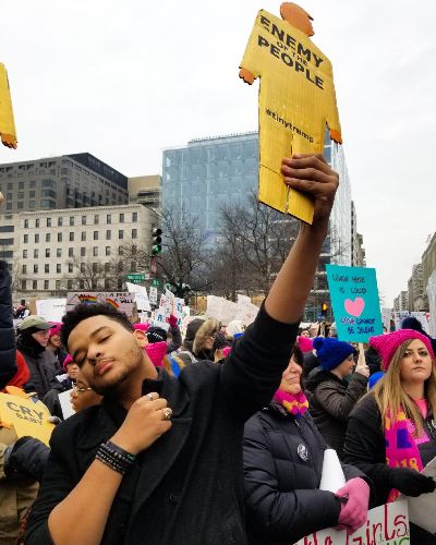 Photograph of a Black male holding a tiny trump high in the air in a sign of defiance