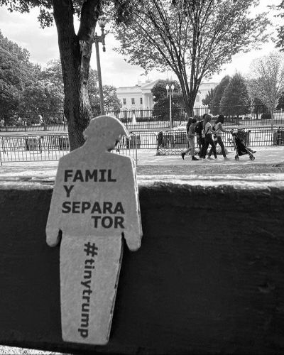 a black and white photo of a tiny trump with the slogan 'Family Separator' in the foreground; children playing in the background