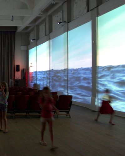 Photograph of dark interior with a body of water projected on both the left and right walls