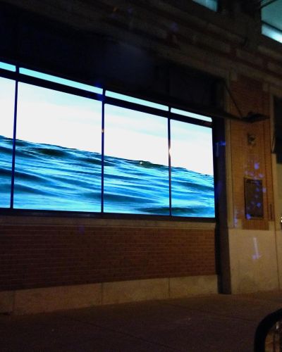 Nighttime photograph of a body of water projected into the storefront windows of a gallery