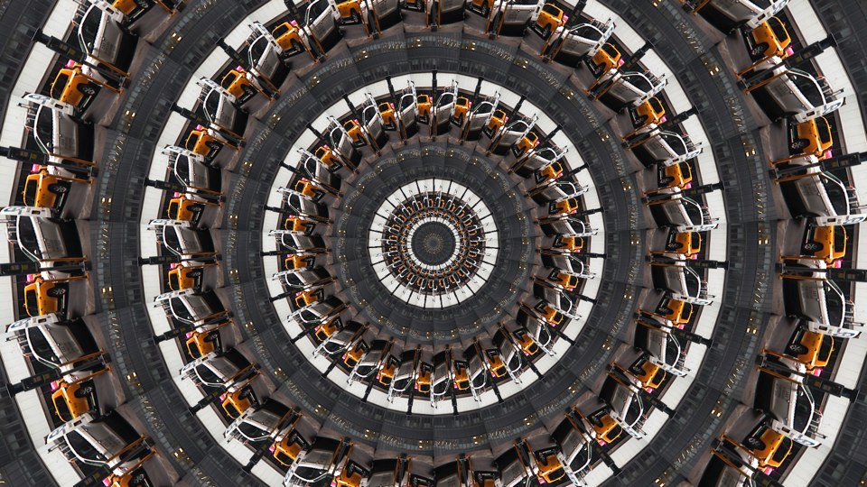 Algorithmically generated kaleidoscopic image consisting of a series of infinite-mirror-esque concentric discs, each one subdivided into multiple tranches that show the same image, albeit rotated by a consistent amount across the disc. In this case, the image that gets repeated across all discs at different angles is a photograph of two parked cars abutting each other, one NYC yellow cab and the other a white van.