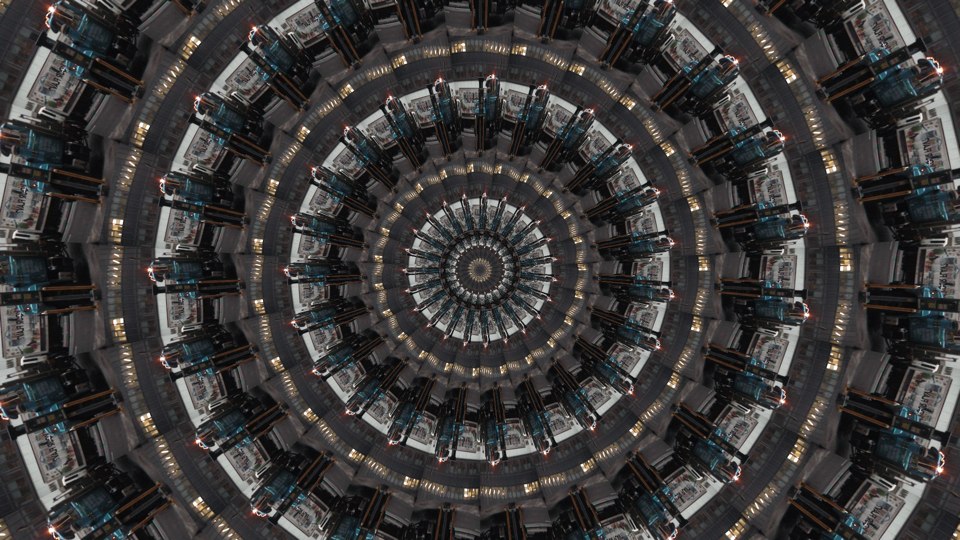 Algorithmically generated kaleidoscopic image consisting of a series of infinite-mirror-esque concentric discs, each one subdivided into multiple tranches that show the same image, albeit rotated by a consistent amount across the disc. In this case, the image that gets repeated across all discs at different angles is a photograph of the blue cab of an 18-wheeler in front of a white delivery van.