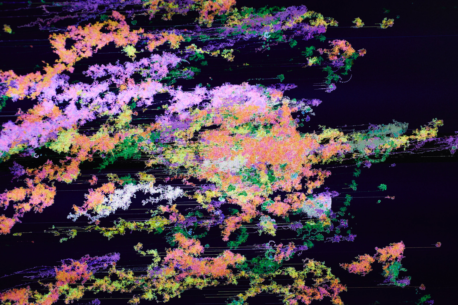 Close-up photograph of the middle of the previous image showing a swirling chaotic mess of multicolored, organically shaped pixel clusters against a deep blue background.