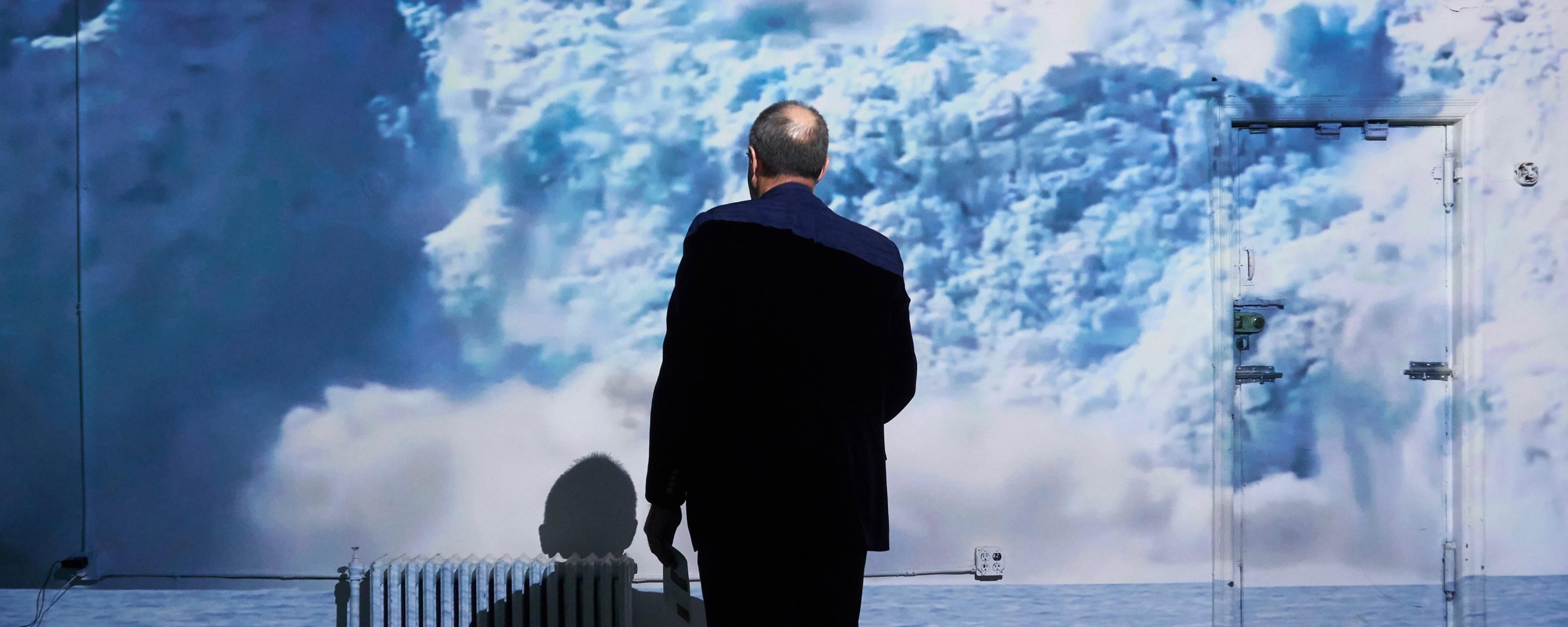Photograph of the back of a man in a suit as he stares at a projection of a giant white glacier in front of him