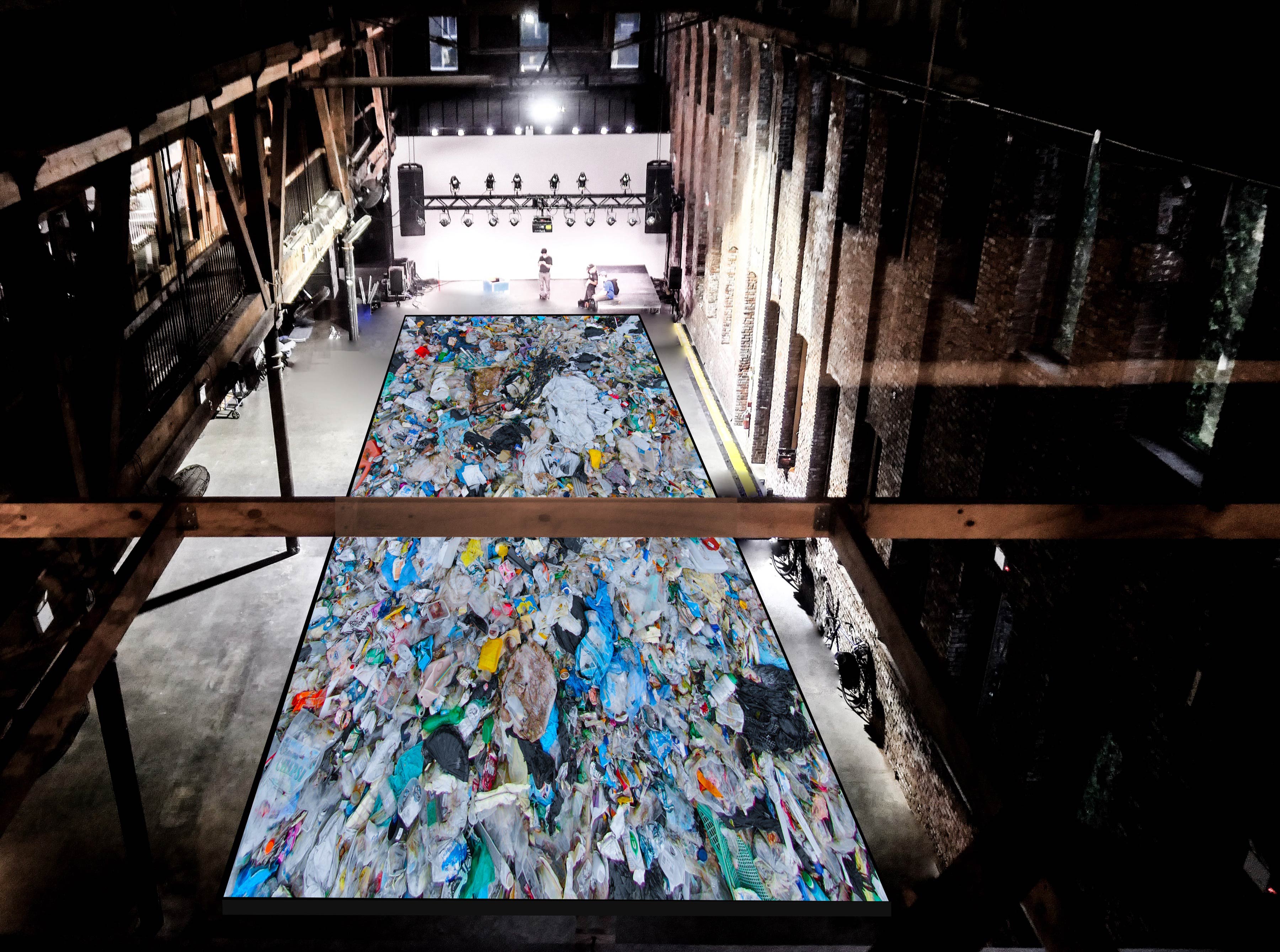 A top-down photograph of a giant, football field-esque gallery space with a giant (2,000 sq feet) rectilinear pool in the middle, packed seemingly thousands of single-use plastic items