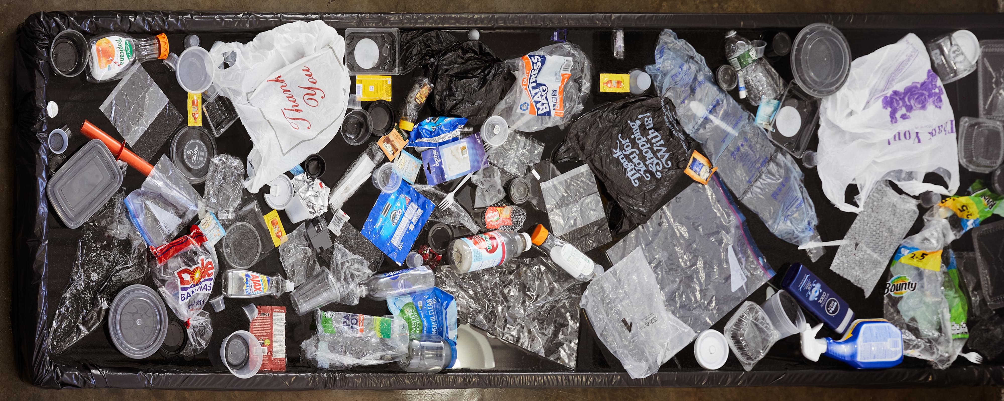 Top-down photograph of collection of about 50 pieces of the artist's single use plastic floating in a small black pool. Most prominently featured are two plastic 'Thank You' shopping bags.