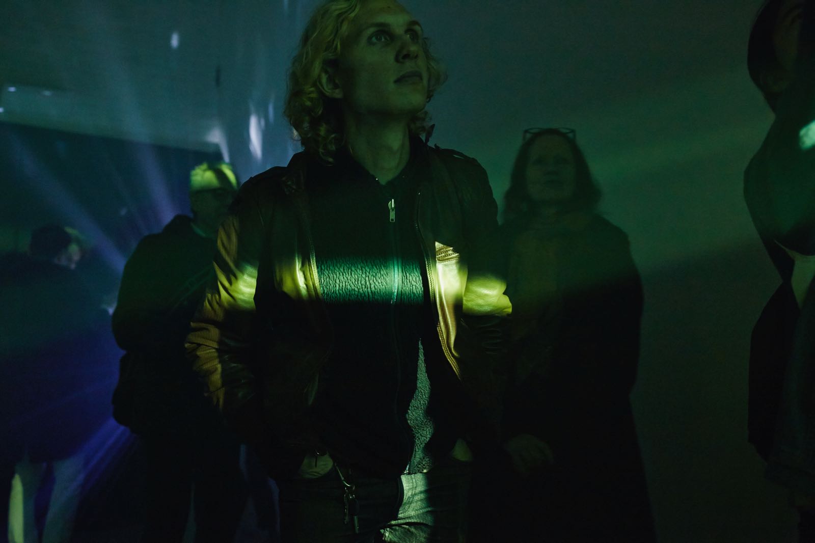 Photograph of a viewer, coated in yellow light with a particularly bright band of yellow light flowing horizontally across his chest, looking upward, with curiosity