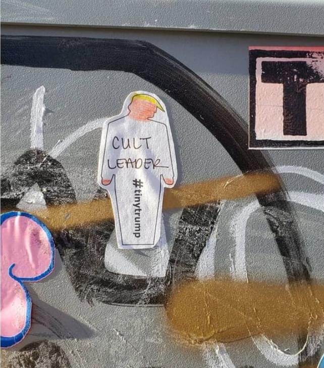 Photograph of a white 'DIY' tiny trump printed on label paper with the words Cult Leader handwritten in pen